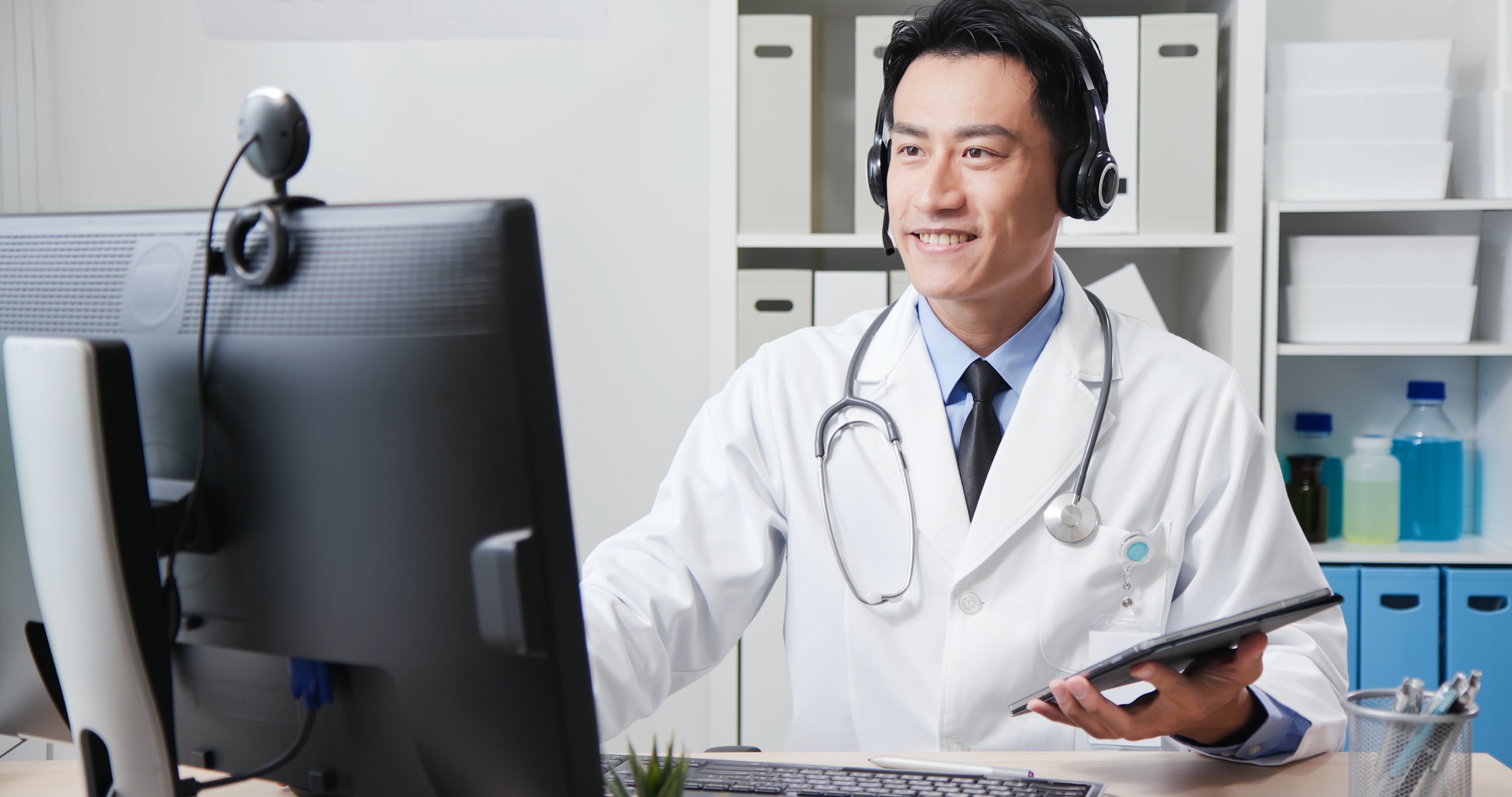 Veterinarian in a clinic conducting a telehealth visit with headset, monitor, and tablet